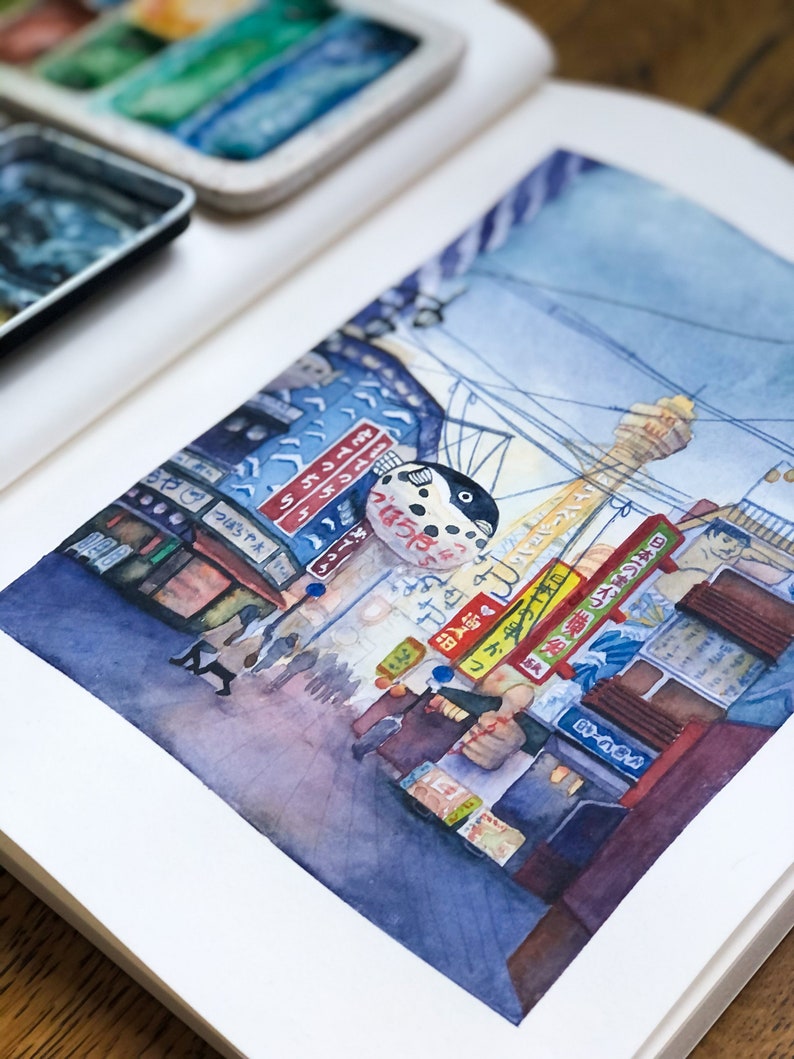 May include: Watercolour painting of a street scene in Japan. The painting features a blue and white pufferfish sign, a tall building, and a street lined with shops and people. The painting is done in a realistic style and captures the vibrant energy of a Japanese city.