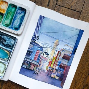 May include: Watercolour painting of a street scene in Japan. The painting features a tall tower, buildings with Japanese signs, and a crowd of people walking down the street. The sky is a light blue with a few clouds.