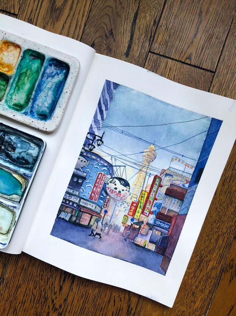 May include: Watercolour painting of a street scene in Japan. The painting features a tall tower, buildings with Japanese signs, and a crowd of people walking down the street. The sky is a light blue with a few clouds.