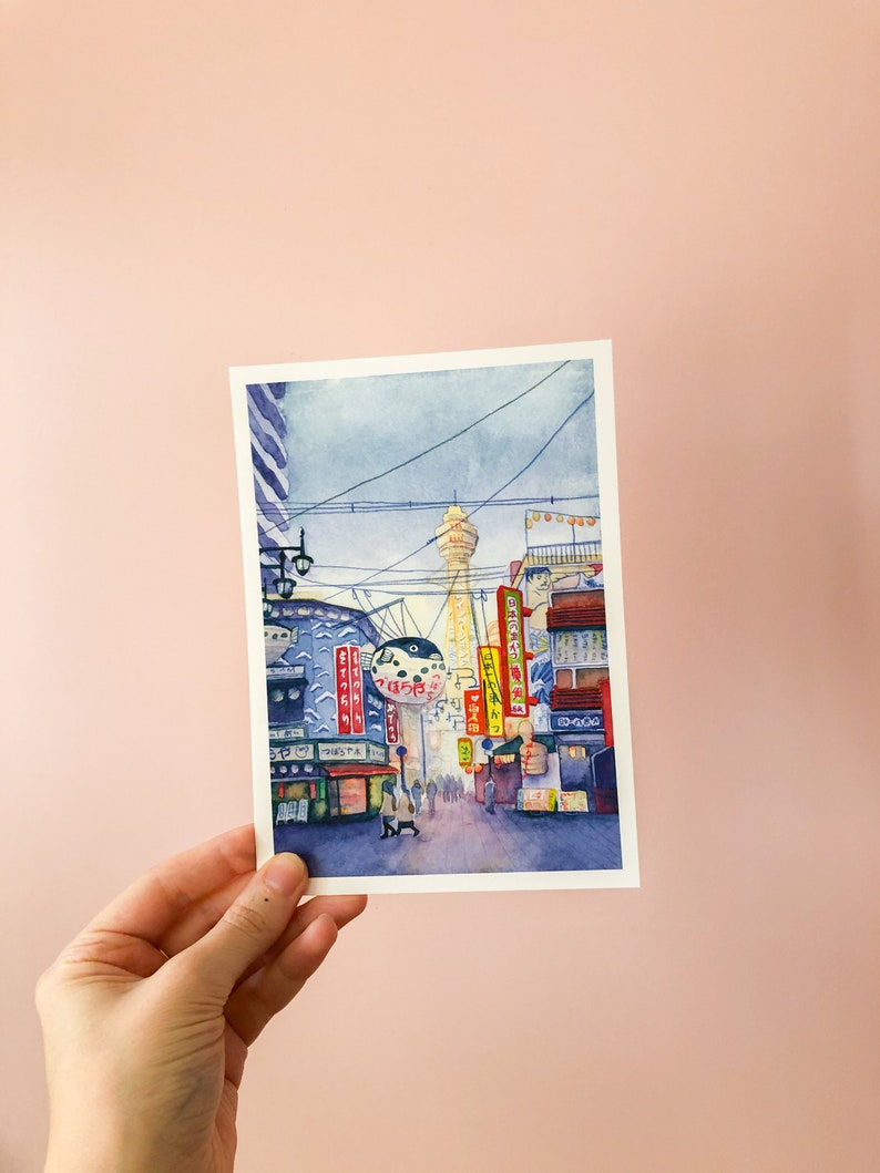 May include: Watercolour painting of a street scene in Japan. The painting features a tall tower in the distance, with buildings and streetlights lining the street in the foreground. The buildings have Japanese characters on them, and there are people walking on the street.