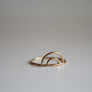 Könnte beinhalten: Ein goldener Ring mit einem einfachen, minimalistischen Design, das eine doppelte Bogenform aufweist.