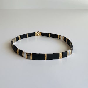 May include: A black and gold bracelet with white and grey beads.