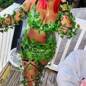 May include: A woman dressed as Poison Ivy for Halloween. She is wearing a green costume with leaves and vines, a red wig, and black boots.