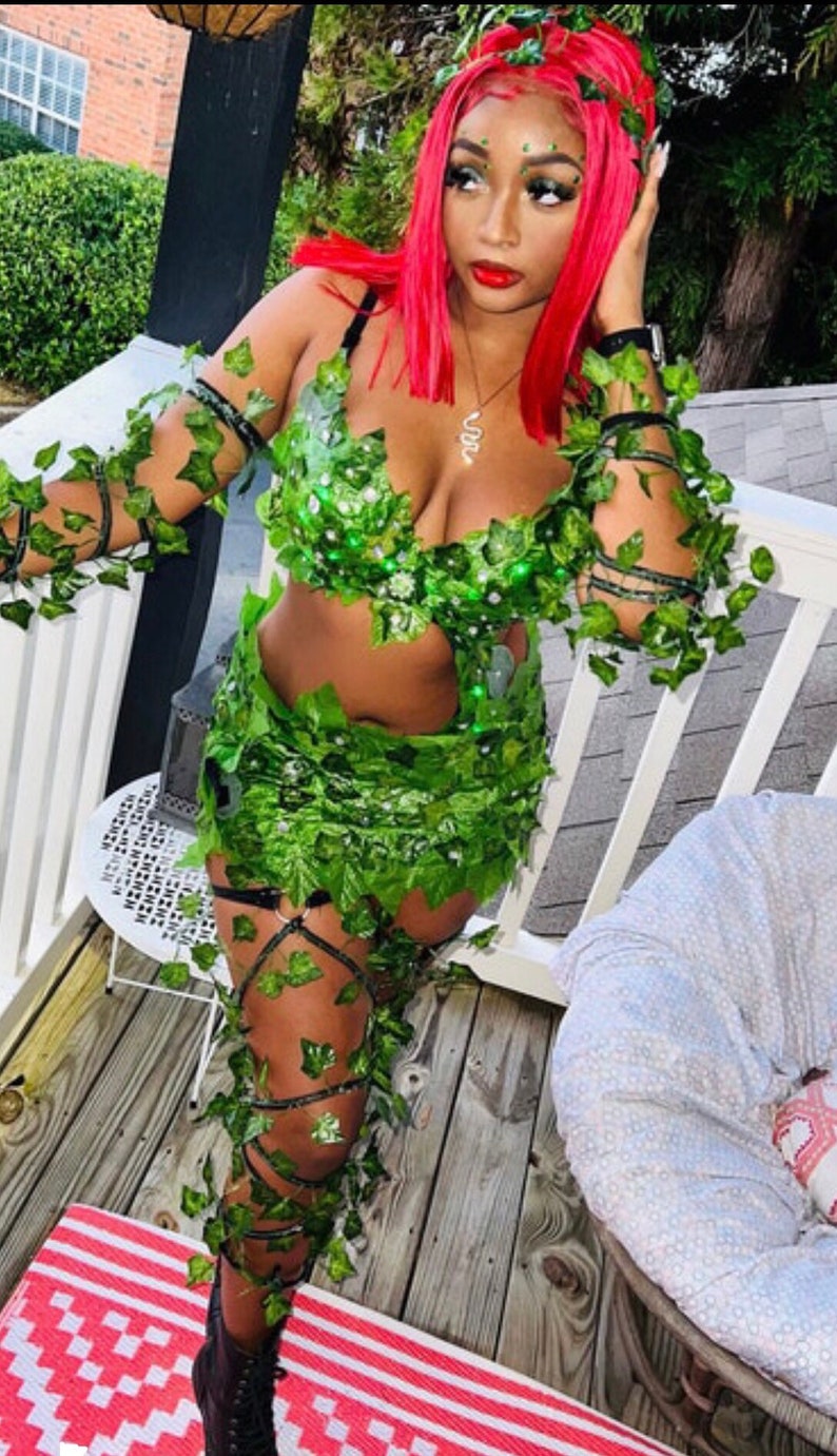 May include: A woman dressed as Poison Ivy for Halloween. She is wearing a green costume with leaves and vines, a red wig, and black boots.