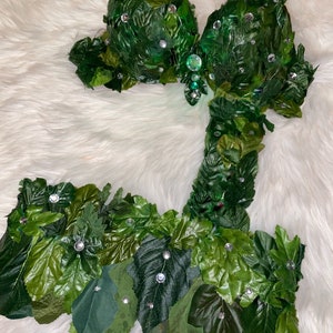 May include: A green leaf bra and skirt costume with rhinestones. The costume is made of green leaves and has a fitted bodice and a flowing skirt.