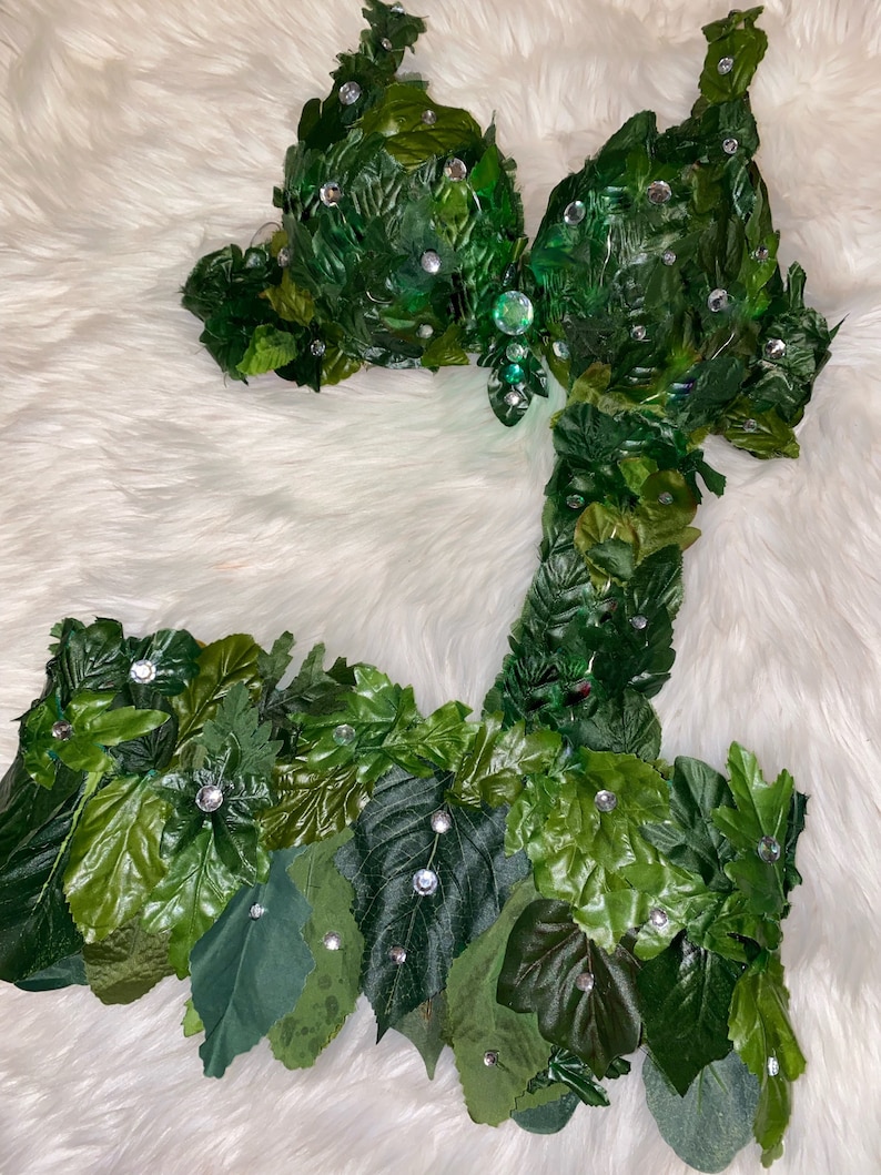 May include: A green leaf bra and skirt costume with rhinestones. The costume is made of green leaves and has a fitted bodice and a flowing skirt.