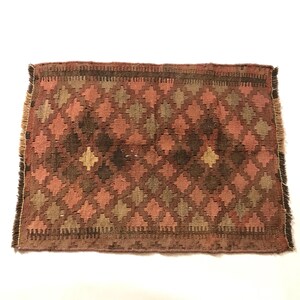 May include: A small, rectangular rug with a geometric pattern in shades of brown, pink, and beige. The rug has a fringed edge.