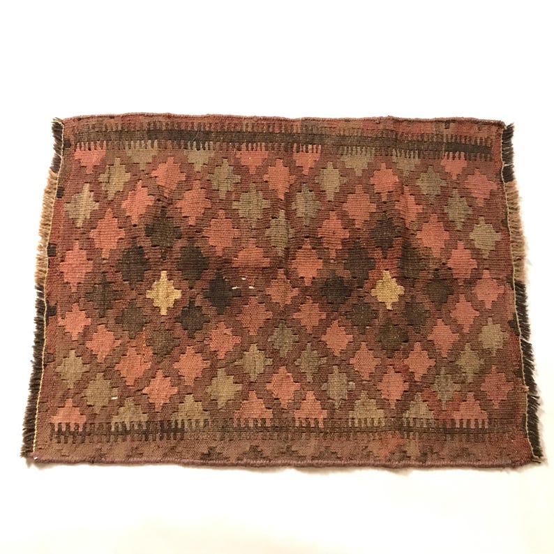 May include: A small, rectangular rug with a geometric pattern in shades of brown, pink, and beige. The rug has a fringed edge.