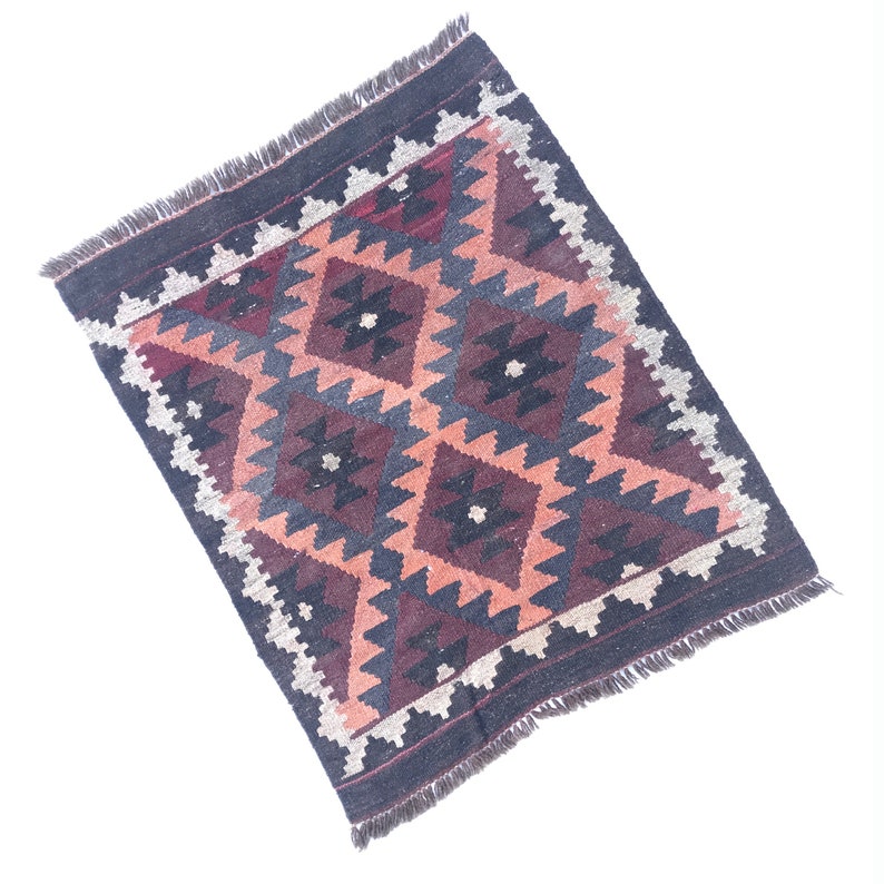 May include: A traditional rug with a geometric pattern in shades of brown, red, and cream. The rug has a fringe border.