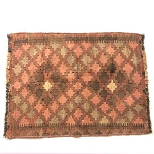 May include: A small, rectangular rug with a geometric pattern in shades of brown, pink, and beige. The rug has a fringed edge.