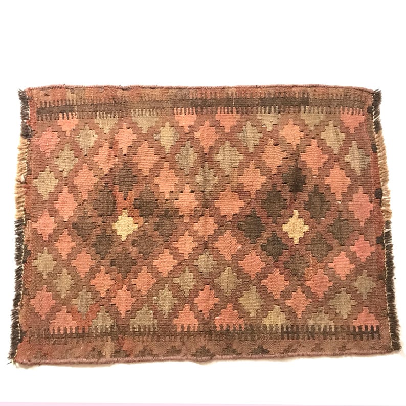 May include: A small, rectangular rug with a geometric pattern in shades of brown, pink, and beige. The rug has a fringed edge.