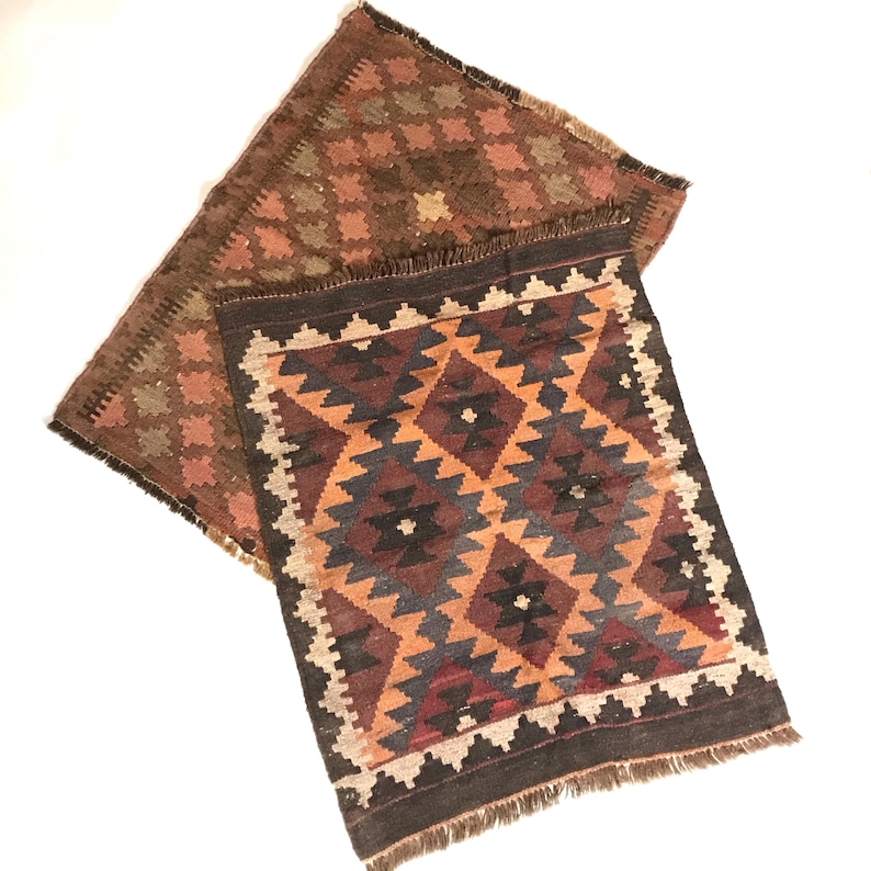 May include: Two woven rugs with geometric patterns in shades of brown, orange, and blue. The rugs have fringed edges.
