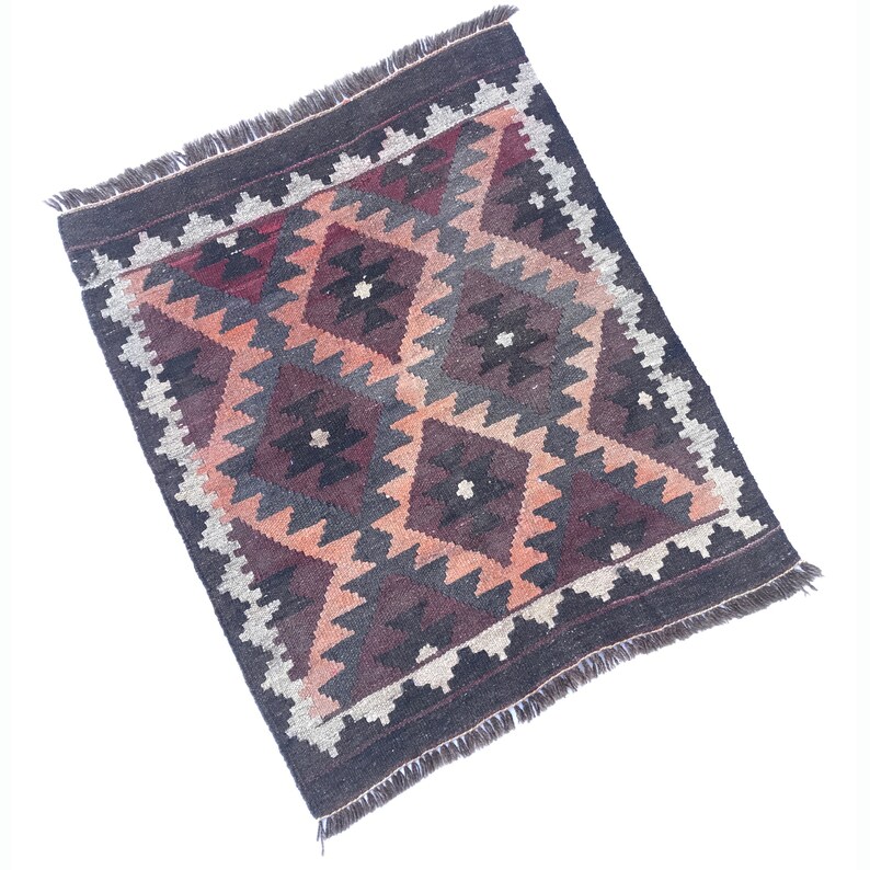 May include: A traditional rug with a geometric pattern in shades of brown, red, and cream. The rug has a fringed border.