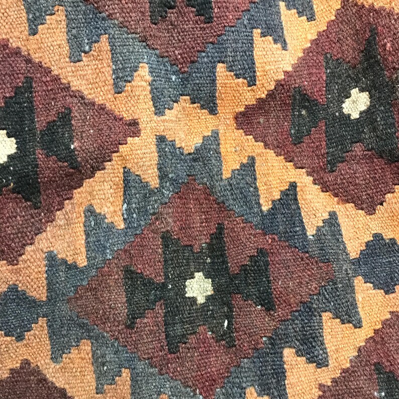 May include: A close-up of a woven rug with a geometric pattern in shades of brown, black, and white. The rug has a traditional design with diamond shapes and intricate details.