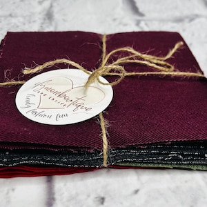 May include: A stack of fabric squares in various colors, including burgundy, black, and red, tied with twine. A white tag with the text "Wymore Boutique" is attached. The fabric appears to be a textured material.