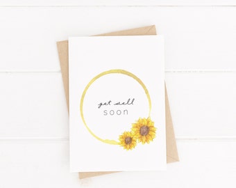 May include: A white card with a gold circle and two yellow sunflowers. The text "get well soon" is written inside the circle.