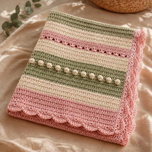 May include: A rectangular crochet blanket featuring horizontal stripes in sage green, cream, and dusty pink. The design includes a row of small raised bobble stitches across a green section and a decorative scalloped edge border in dusty pink.