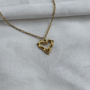May include: A gold chain necklace with a heart-shaped pendant. The heart is made of a detailed, intricate design that resembles flames.