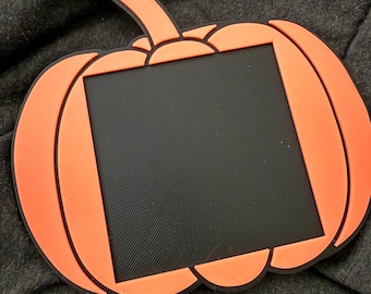 May include: Orange pumpkin-shaped picture frame with a black center. The frame has a black outline and a stem. The frame is made of a rubbery material. Perfect for Halloween or fall decor.