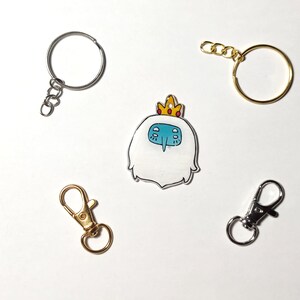 May include: A set of four keychains featuring a cartoon character with a crown, a silver key ring, a gold key ring, and a silver lobster clasp.