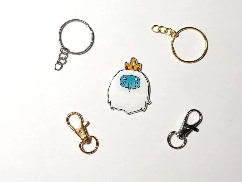 May include: A set of four keychains featuring a cartoon character with a crown, a silver key ring, a gold key ring, and a silver lobster clasp.
