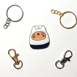 May include: A white and blue cartoon character keychain with a gold chain and a silver split ring. There are two additional silver split rings and a gold lobster clasp.