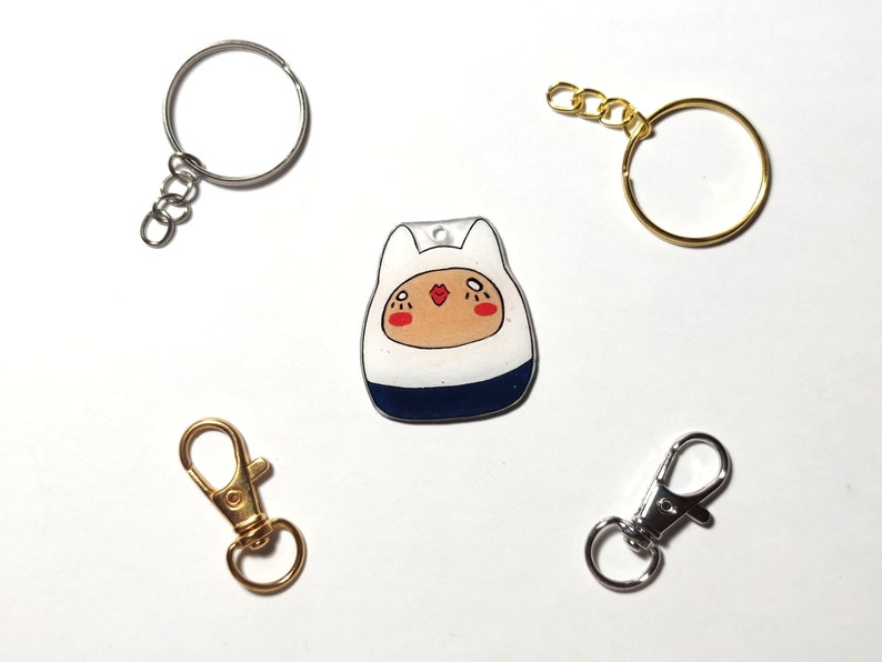 May include: A white and blue cartoon character keychain with a gold chain and a silver split ring. There are two additional silver split rings and a gold lobster clasp.