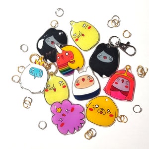 May include: A set of 10 colorful cartoon character keychains featuring characters from the animated television series Adventure Time. The keychains are made of clear acrylic and feature a variety of characters, including Finn, Jake, Princess Bubblegum, Marceline, and Ice King.