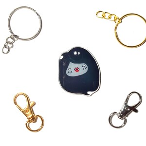 May include: Four keychains with different styles. One keychain is a silver circle with a silver chain. Another keychain is a gold circle with a gold chain. The third keychain is a silver lobster clasp. The fourth keychain is a black and white enamel pin of a cartoon character with a red mouth.