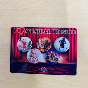 May include: Five round buttons with images of popular musicals. The buttons are red, blue, yellow, white, and purple. The text on the buttons reads "Heathers", "Bat Out of Hell", "Matilda", "Waitress", and "Aladdin". The buttons are on a red and white stage curtain with the text "I love Musical Theatre" above the buttons.