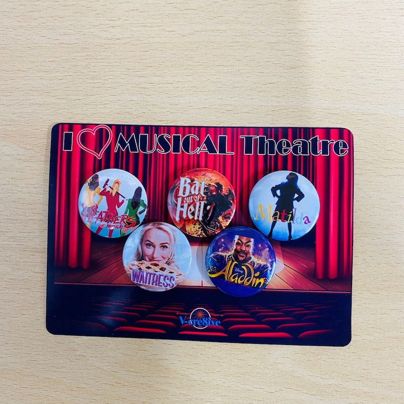 May include: Five round buttons with images of popular musicals. The buttons are red, blue, yellow, white, and purple. The text on the buttons reads "Heathers", "Bat Out of Hell", "Matilda", "Waitress", and "Aladdin". The buttons are on a red and white stage curtain with the text "I love Musical Theatre" above the buttons.