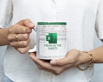 Könnte beinhalten: Eine weiße Keramiktasse mit einem grün-weißen Design, das das Microsoft Excel-Logo und den Text "Freak in the Sheets" zeigt.