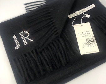 May include: A black scarf with fringed edges and the initials "JR" in rhinestones. The scarf has a tag that reads "LUZ fair trade" and "luzfairtrade.com".
