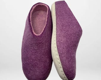 Può includere: Un paio di pantofole in feltro viola. Le pantofole hanno un interno rosa chiaro e una suola bianca. Le pantofole sono realizzate in un materiale morbido e strutturato. Sono progettate per l'uso in casa.