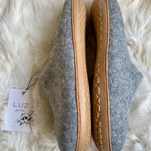 Puede incluir: Un par de zapatillas de lana grises con suelas de cuero marr&oacute;n. Las zapatillas tienen una suela texturizada y son de la marca Luz.