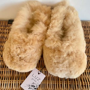 Op de afbeelding: Een paar beige wollen pantoffels met een label met de tekst "LUZ fair trade".