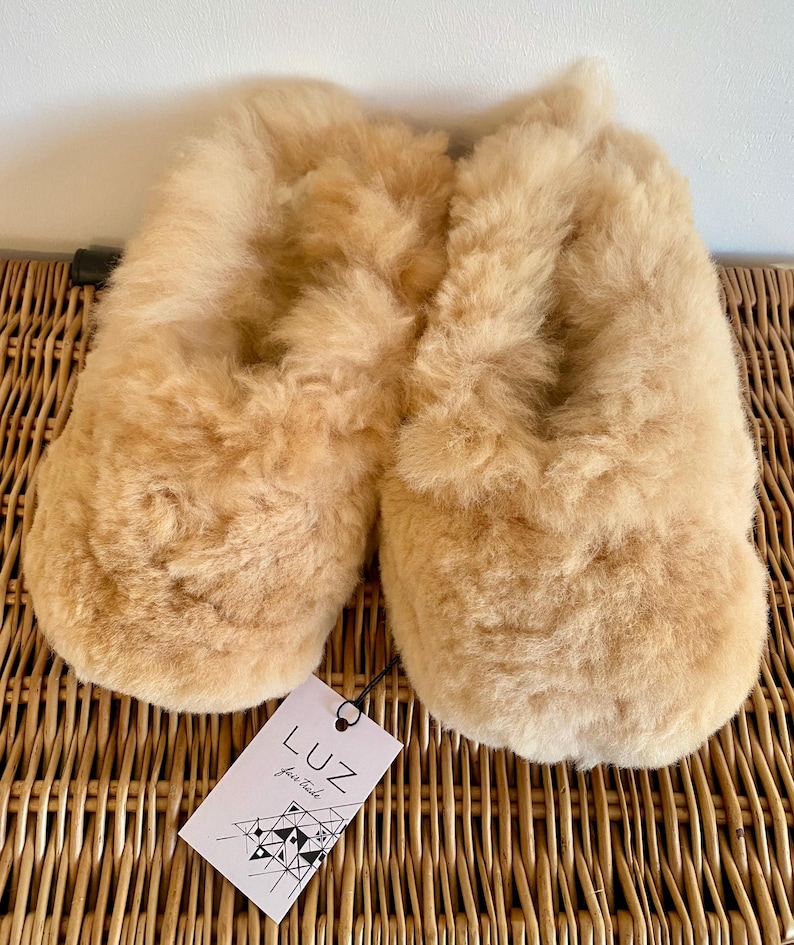 Op de afbeelding: Een paar beige wollen pantoffels met een label met de tekst "LUZ fair trade".