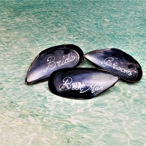 May include: Three black seashells with the words "Bride", "Groom", and "Best Man" inscribed in white.