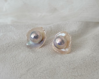 May include: A pair of pearl earrings. Each earring features a large, iridescent pearl set within a delicate, petal-like frame. The pearls have a lustrous, silvery sheen, and the frames are a soft, creamy white.