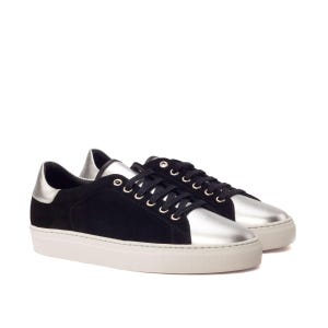 May include: A pair of low-top sneakers featuring a combination of black suede and metallic silver leather panels. The shoes include black laces, silver-toned metal eyelets, and a thick white rubber sole with a textured edge for traction.