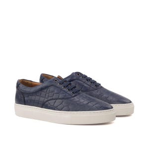 May include: A pair of low-top sneakers in dark navy blue with a textured crocodile-embossed leather upper. The shoes feature matching navy blue laces, silver-toned metal eyelets, and a thick, solid white rubber sole with a textured sidewall.