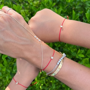 May include: A collection of bracelets including several thin red cord bracelets with a single small round diamond, a delicate gold chain bracelet with three small diamonds, a silver-toned tennis bracelet, and a gold bangle with screw motifs.