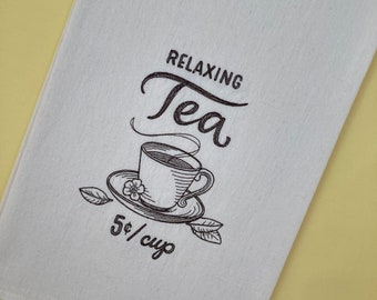 May include: White tea towel with black embroidery of a teacup and saucer with steam rising from the cup. The text "Relaxing Tea 5¢/cup" is embroidered below the teacup.