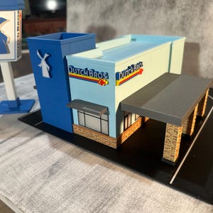 May include: A white ceramic mug with a black handle and the text "But First, Coffee" in a black, bold font. The mug is sitting on a wooden surface. The mug is approximately 4 inches tall.