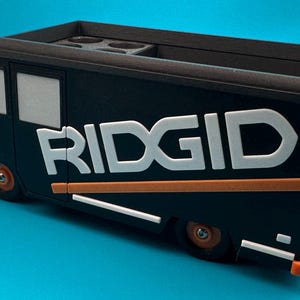 K&ouml;nnte beinhalten: Ein schwarz-oranger Ridgid-Organizer in Form eines Lastwagens. Der LKW hat wei&szlig;e Schriftz&uuml;ge und orangefarbene Akzente. Die R&auml;der und Sto&szlig;stangen sind orange. Die Oberseite des LKWs hat mehrere kreisf&ouml;rmige F&auml;cher.