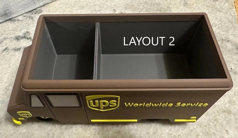 K&ouml;nnte beinhalten: Ein brauner und gelber UPS-Truck-f&ouml;rmiger Organizer mit zwei F&auml;chern. Der Text "LAYOUT 2" ist im Inneren des Organizers sichtbar. Das UPS-Logo und "Worldwide Service" sind auf der Seite aufgedruckt.