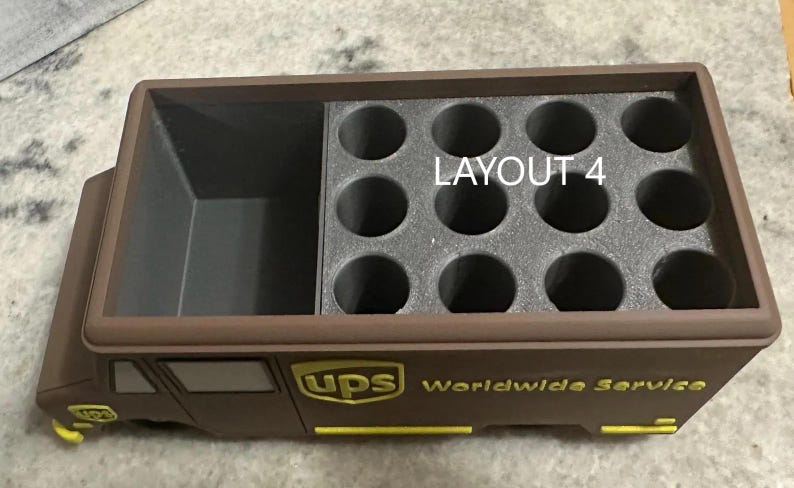 K&ouml;nnte beinhalten: Ein brauner UPS-LKW-f&ouml;rmiger Beh&auml;lter mit einem Staufach und einem Abschnitt mit kreisf&ouml;rmigen L&ouml;chern. Der Text "LAYOUT 4" ist sichtbar. Das UPS-Logo und "Worldwide Service" sind gelb gedruckt.