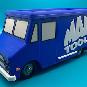 May include: A blue toy truck with the "MAC TOOLS" logo in white on the side. The truck has a white bumper and windows. The toy truck is a miniature replica of a service vehicle.