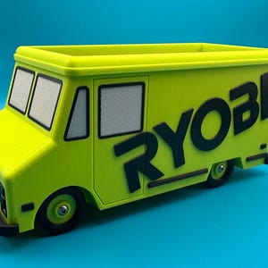 May include: A lime green toy food truck with black accents and the word "RYOBI" in large black letters on the side. The truck has black wheels, windows, and a black front bumper. The truck is sitting on a blue surface.