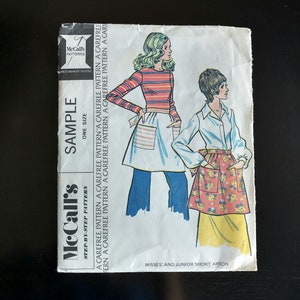 May include: A vintage McCall's sewing pattern for a short apron. The pattern is for misses' and junior sizes. The pattern includes a step-by-step guide and is labeled "Carefree Pattern".